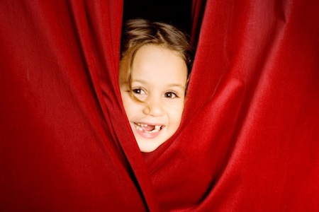 Girl peeking out from behind a stage curtain